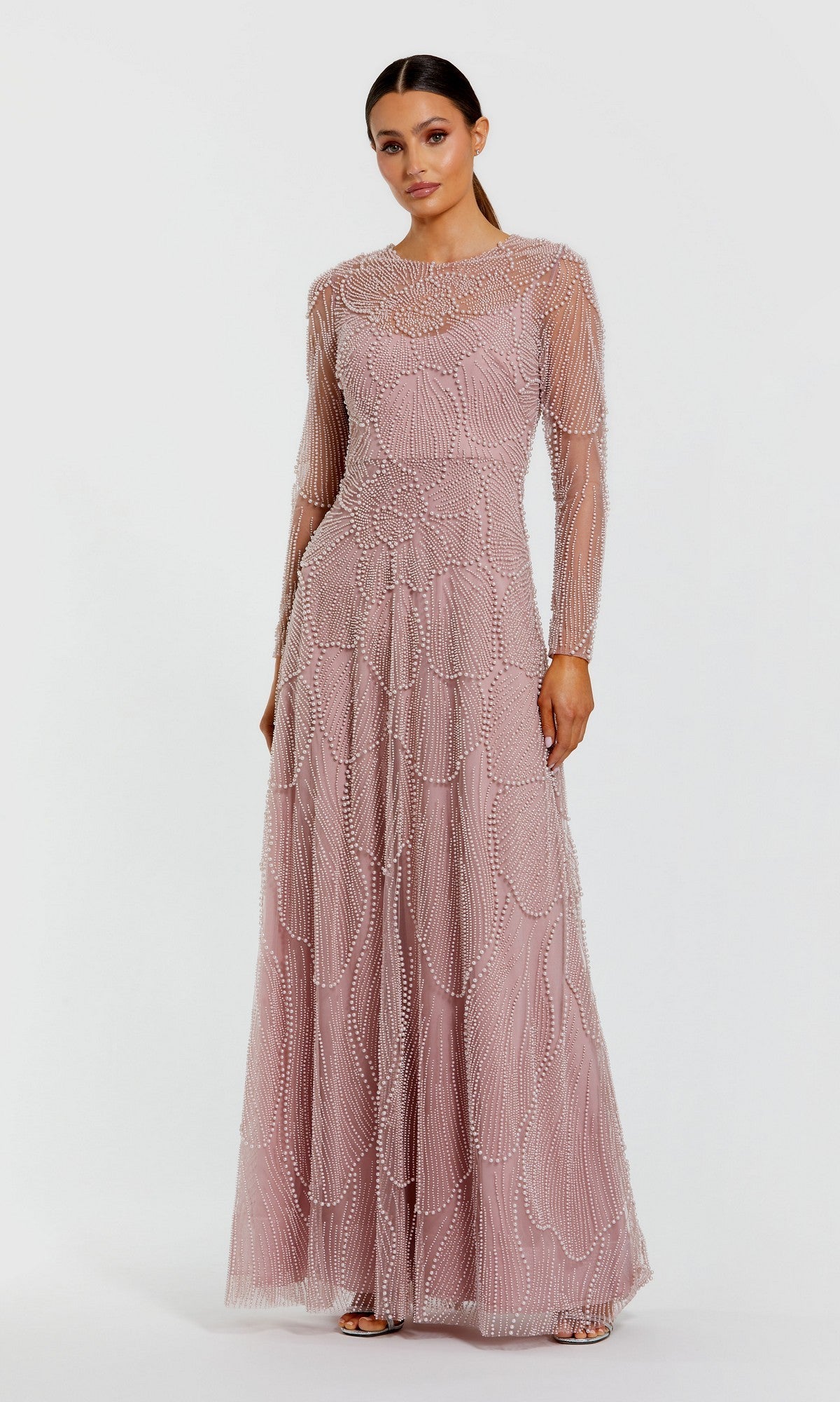 A woman wearing the Mac Duggal 69012 long formal dress in mocha, featuring sheer long sleeves and intricate pearl beaded patterns, stands against a plain white background.